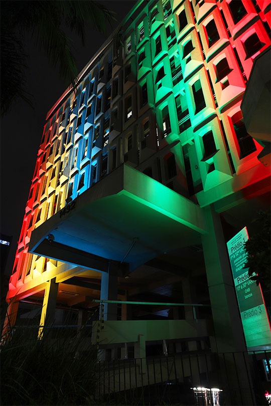 Fachada do Foro trabalhista de Porto Alegre. Foto mostra o prédio iluminado com listras verticais em vermelho, amarelo, azul e verde.