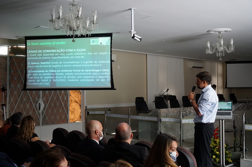 Imagem do servidor Diogo Grimberg durante a apresentação, tendo o público em primeiro plano e, ao fundo, o telão.