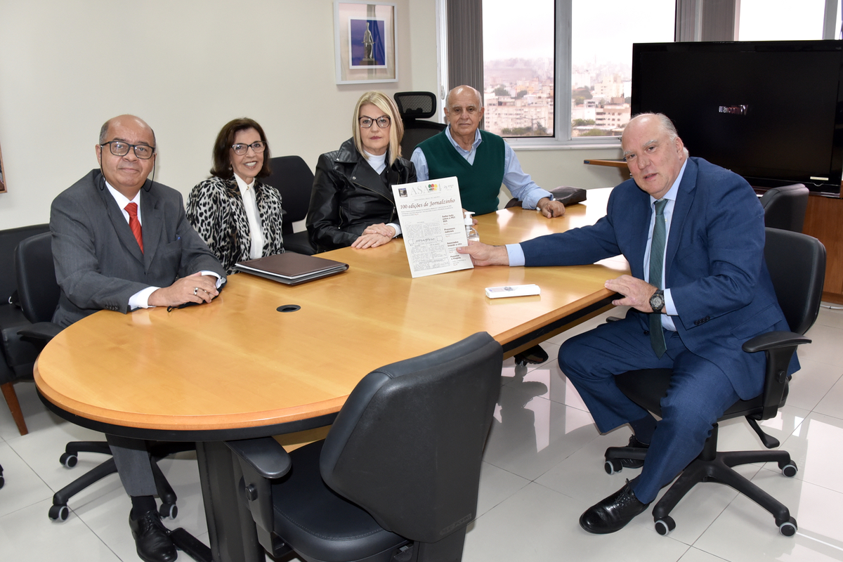 Representantes da ASA-4 sentados à mesa com o vice-presidente Martins Costa, que está segurando um exemplar do informativo da associação.