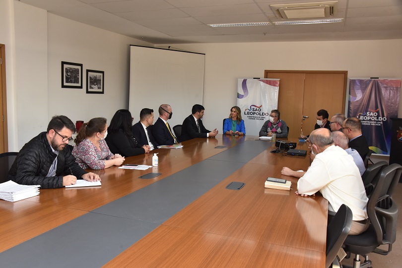 Foto em ângulo aberto da reunião, mostrando mesa e participantes