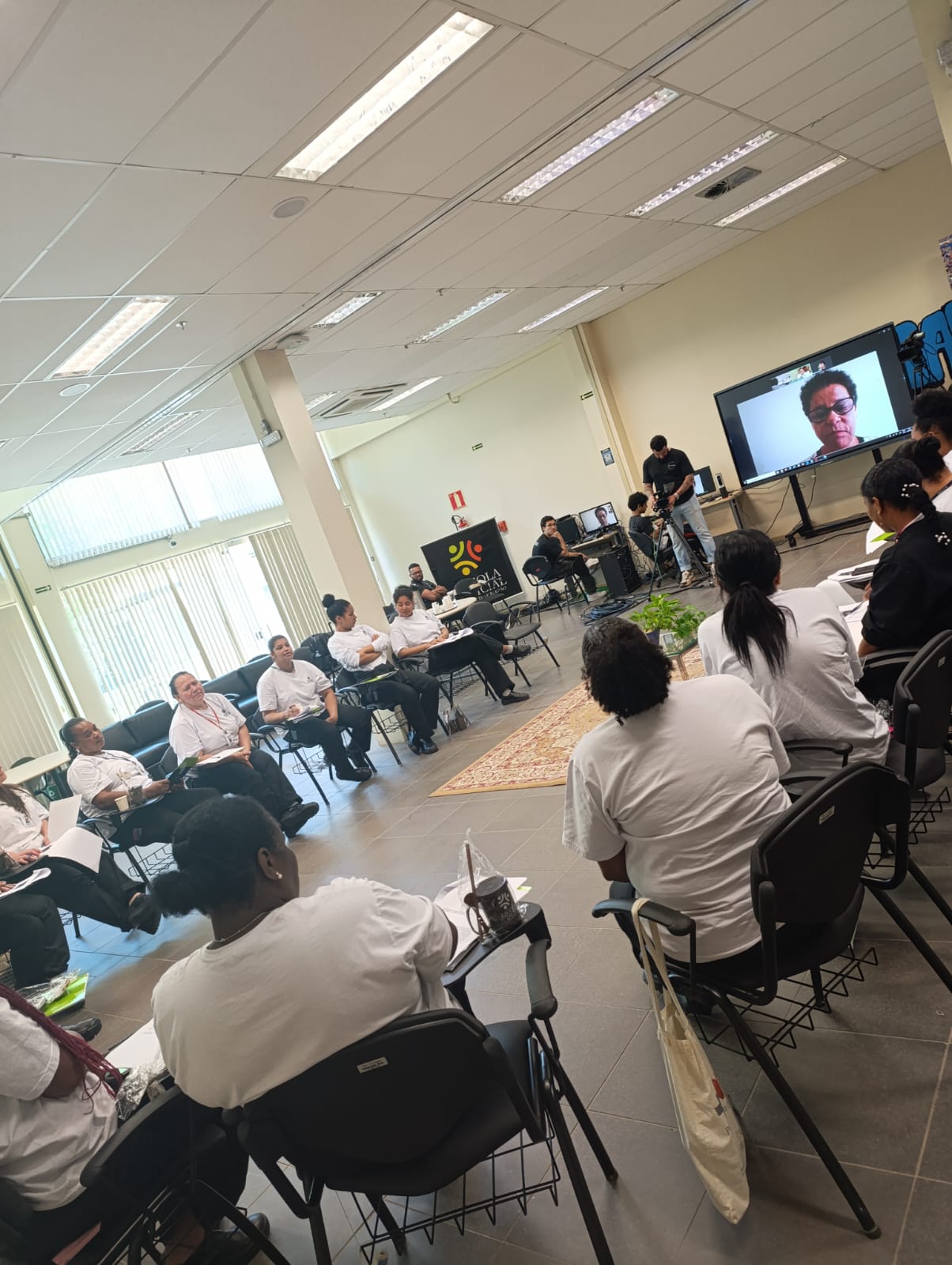 Grupo de alunas participando da oficina, assistindo a docente por meio de telão.