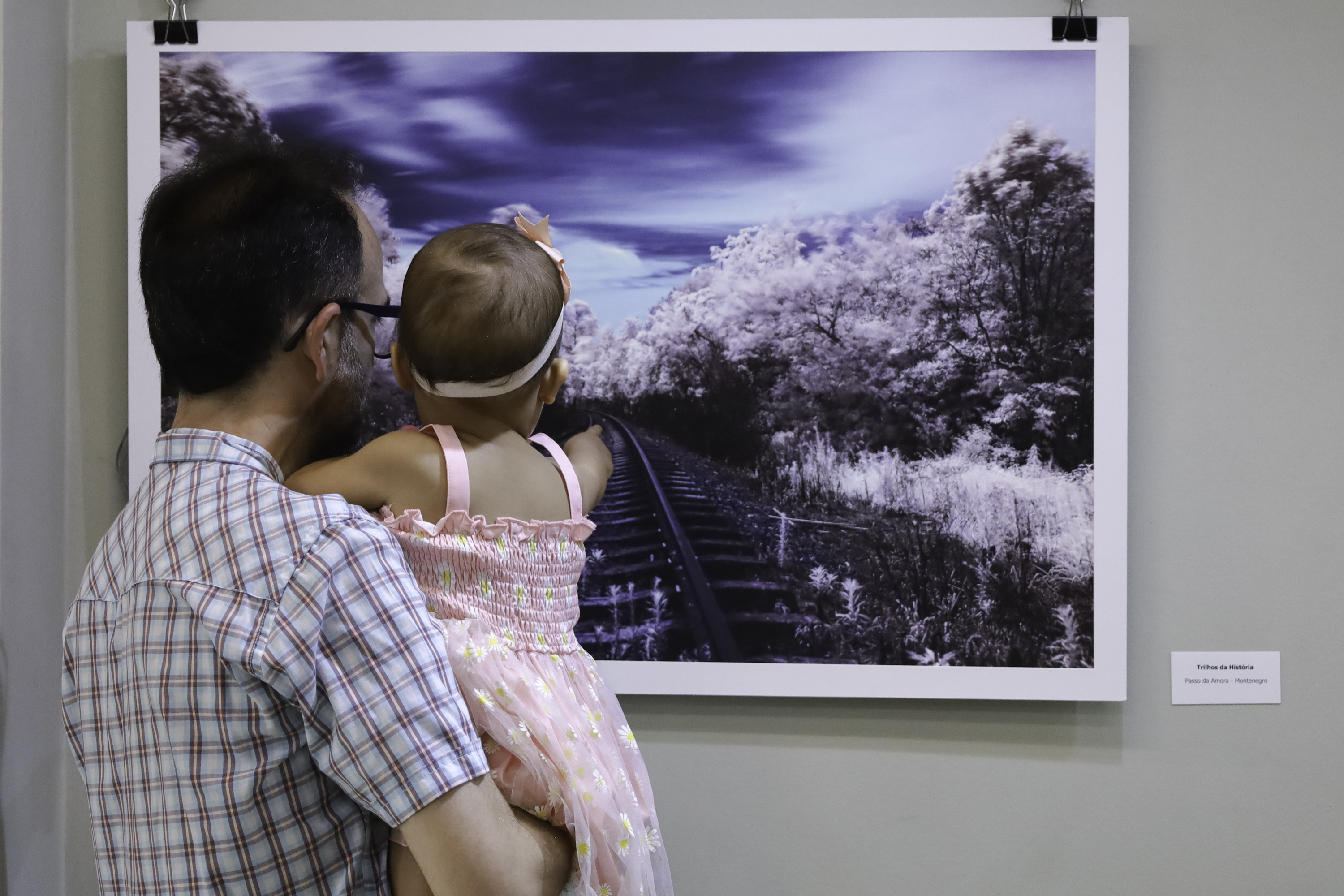 Home com bebê no colo contempla um quadro