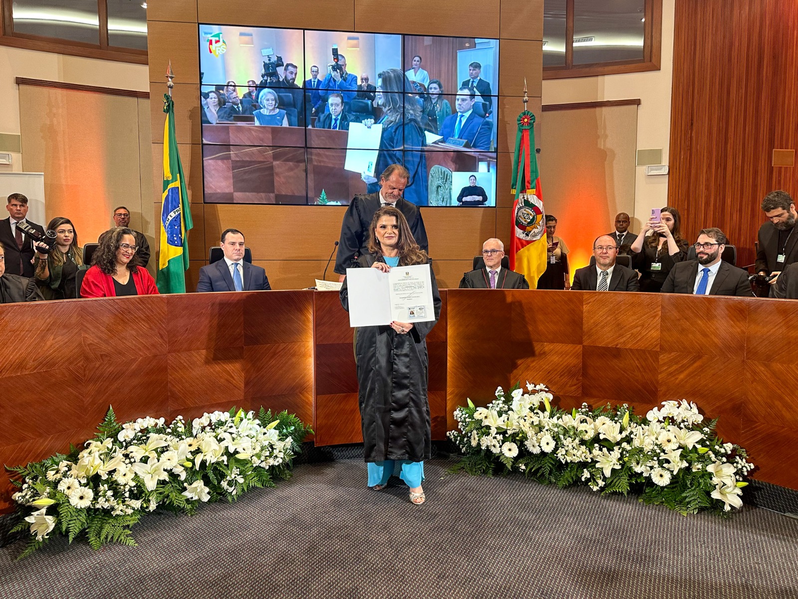 A foto desembargadora com diploma e mesa.