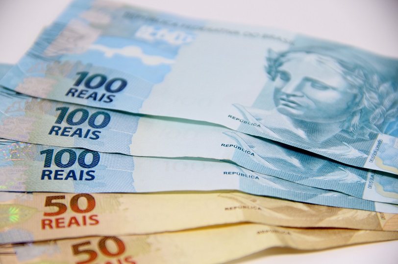 Cédulas de R$ 50 (amarelas) e de R$ 100 (azuis) dispostas sobre bancada branca.