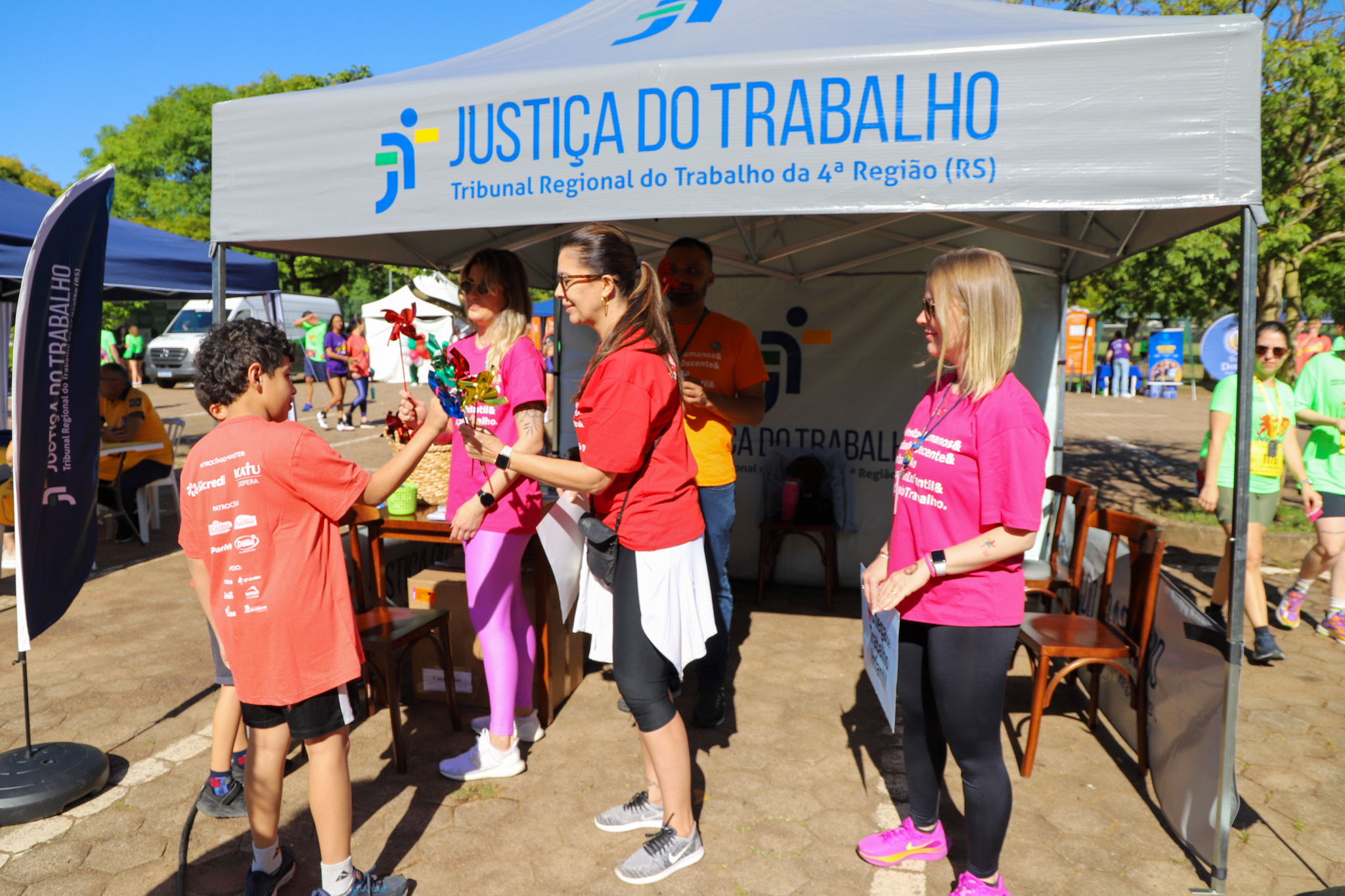 Juíza Aline entrega catavento a criança no estante do TRT-RS na Maratona