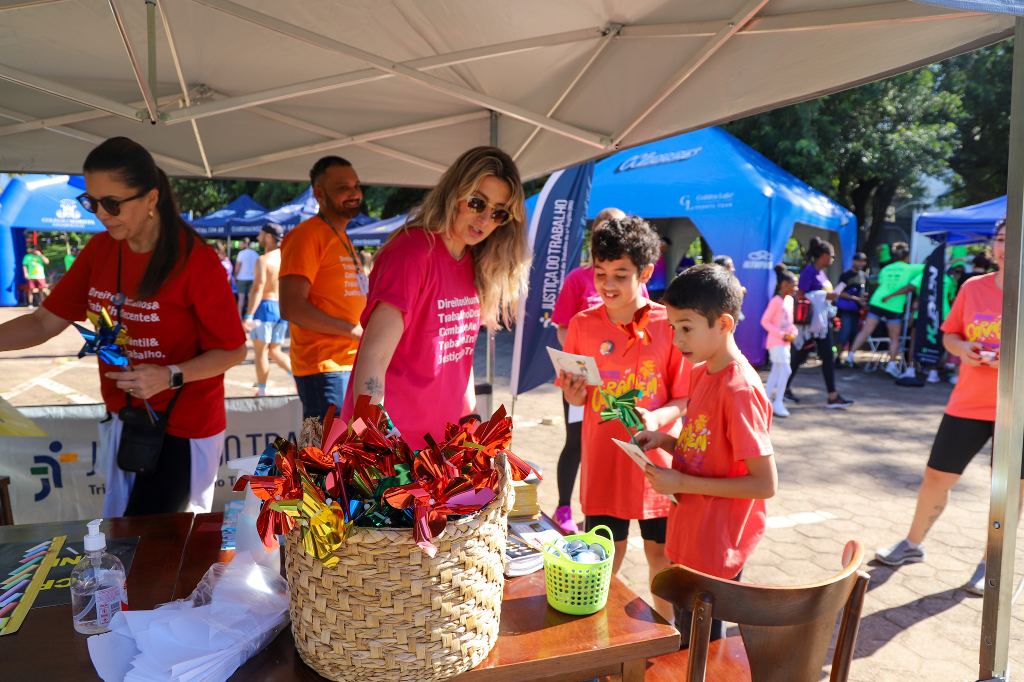 Servidora entrega cataventos a crianças no estande do TRT-RS na maratona