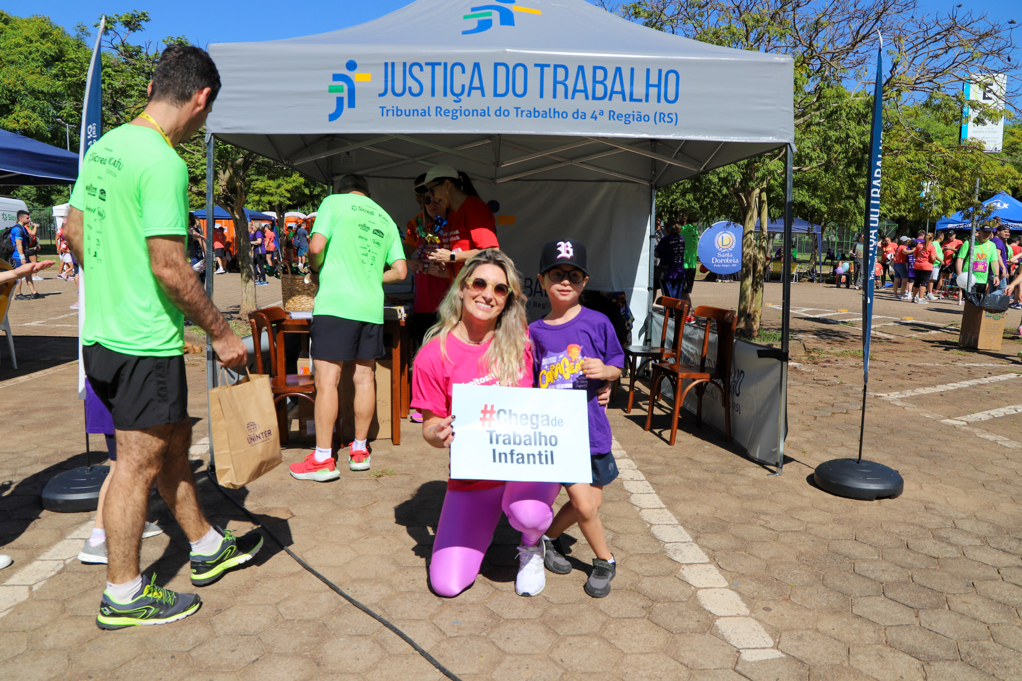 Servidora do TRT-RS posa ao lado de criança maratonista com o cartaz #chega de trabalho infantil