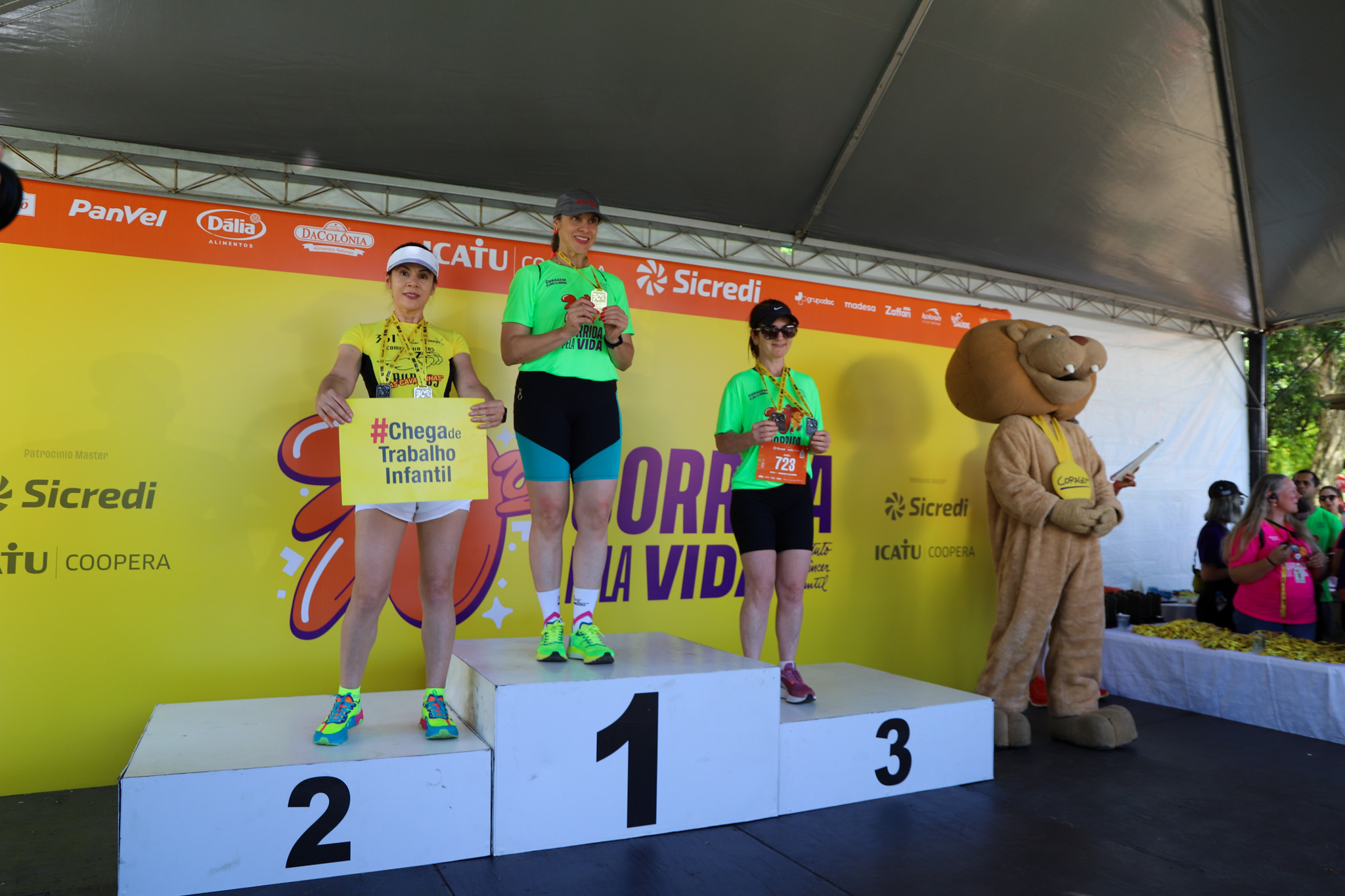 Pódio da Maratona feminina. Há uma corredora com o cartaz #chega de trabalho infantil.