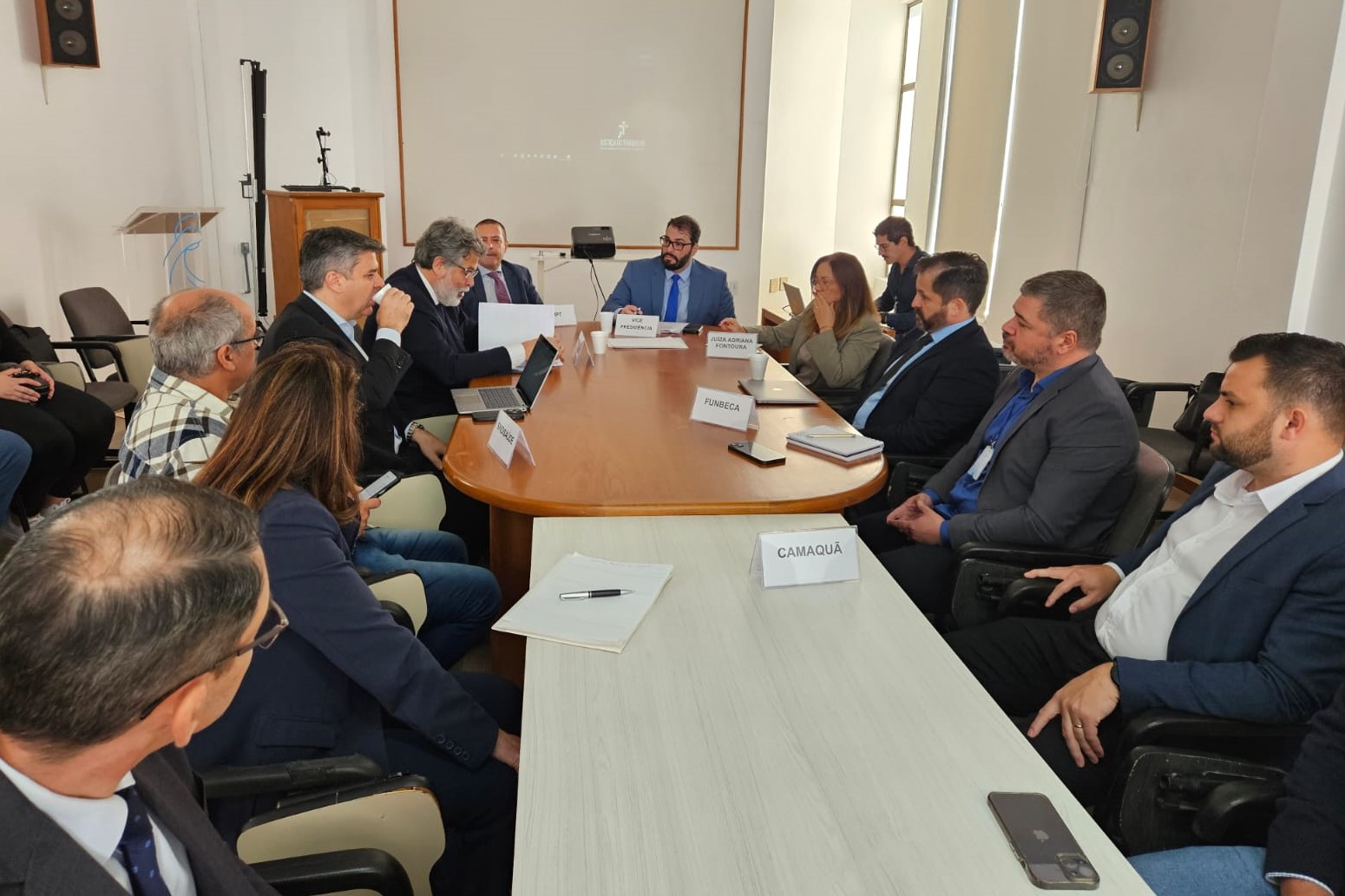 Fotos dos participantes da mediação sentados em volta da mesa de negociação. O vice-presidente Alexandre aparece ao fundo, no centro da foto.