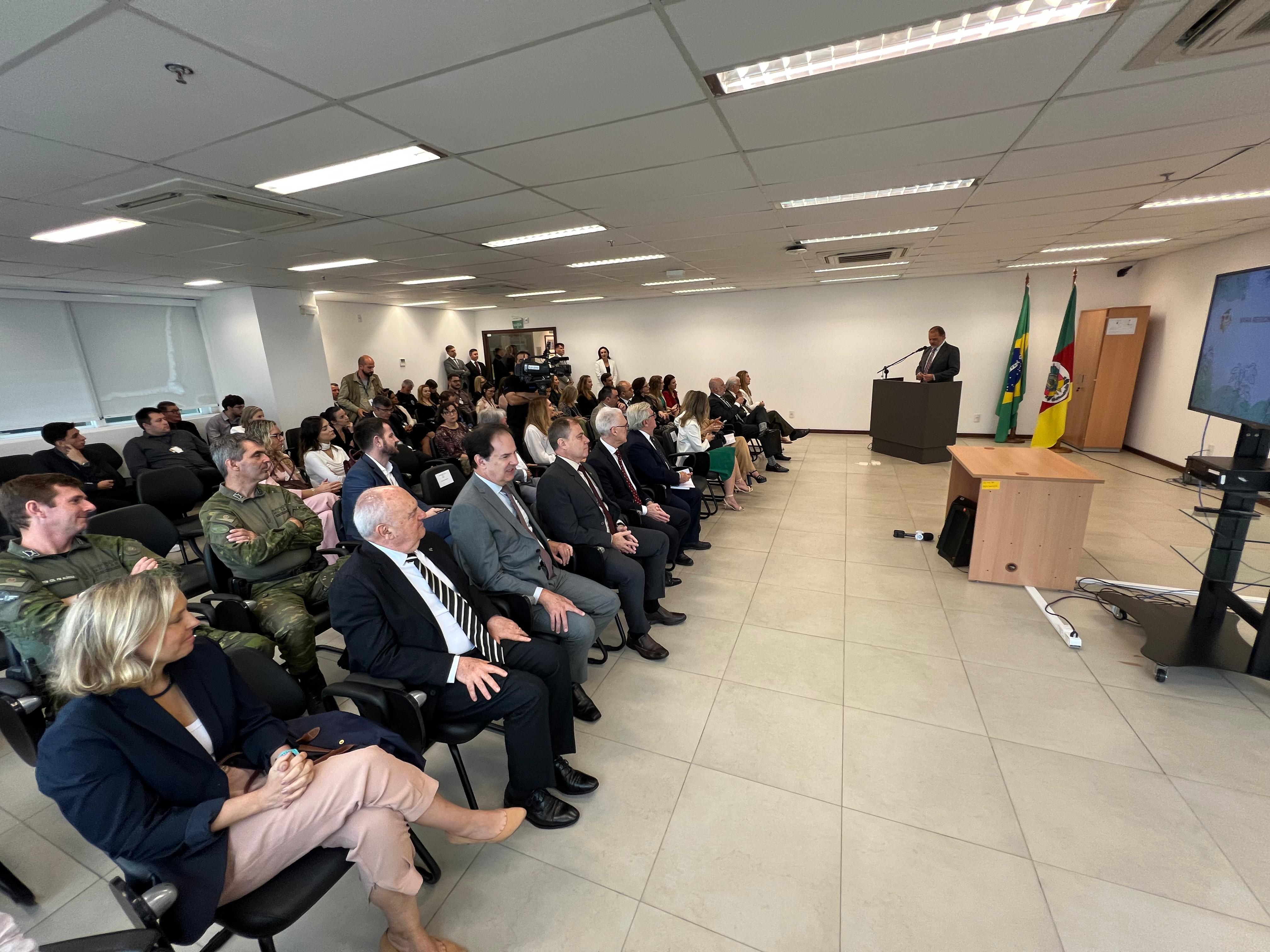 Foto em ângulo aberto, mostrando o público sentado, em primeiro plano. Ao fundo, o presidente do TJ/RS discursando.