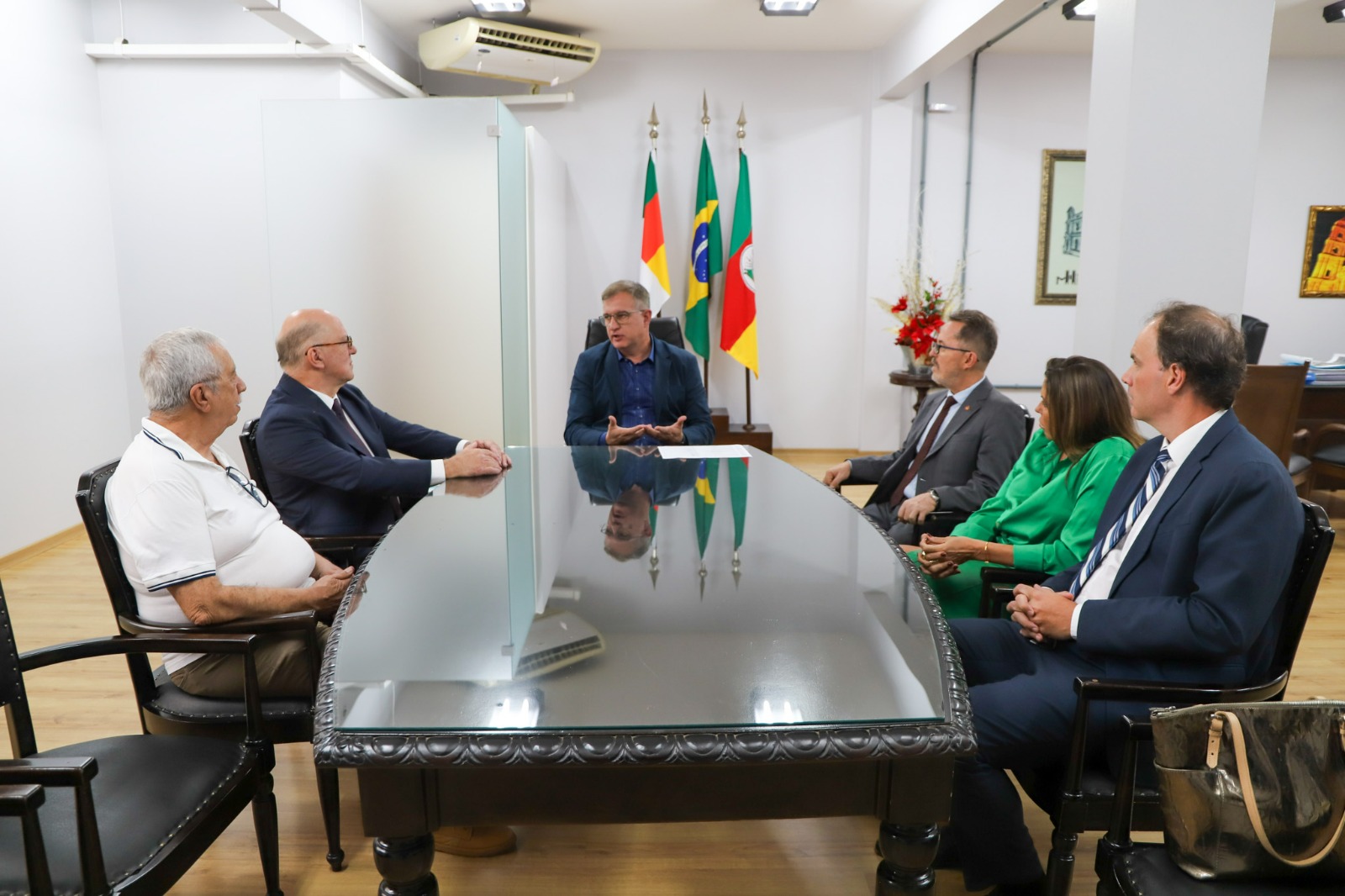 Imagem de Martins Costa participando de uma reunião com outras pessoas numa mesa retangular. É na Prefeitura de Santo Ângelo.
