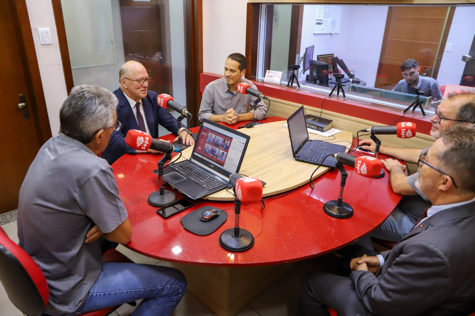 Imagem do desembargador Martins Costa participando de programa de rádio Panorama Debates, na Rádio Sepé. Está debatendo em uma mesa redonda com outras pessoas.