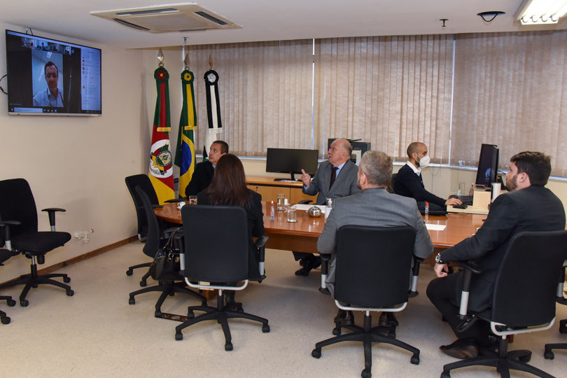 Participantes da mediação na mesa. O Vice-presidente está falando com alguém que participa por videoconferência, que aparece em um TV na esquerda da imagem.