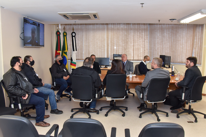 Participantes da mediação na mesa. Aparece um participante por videoconferência, na TV à esquerda da imagem.