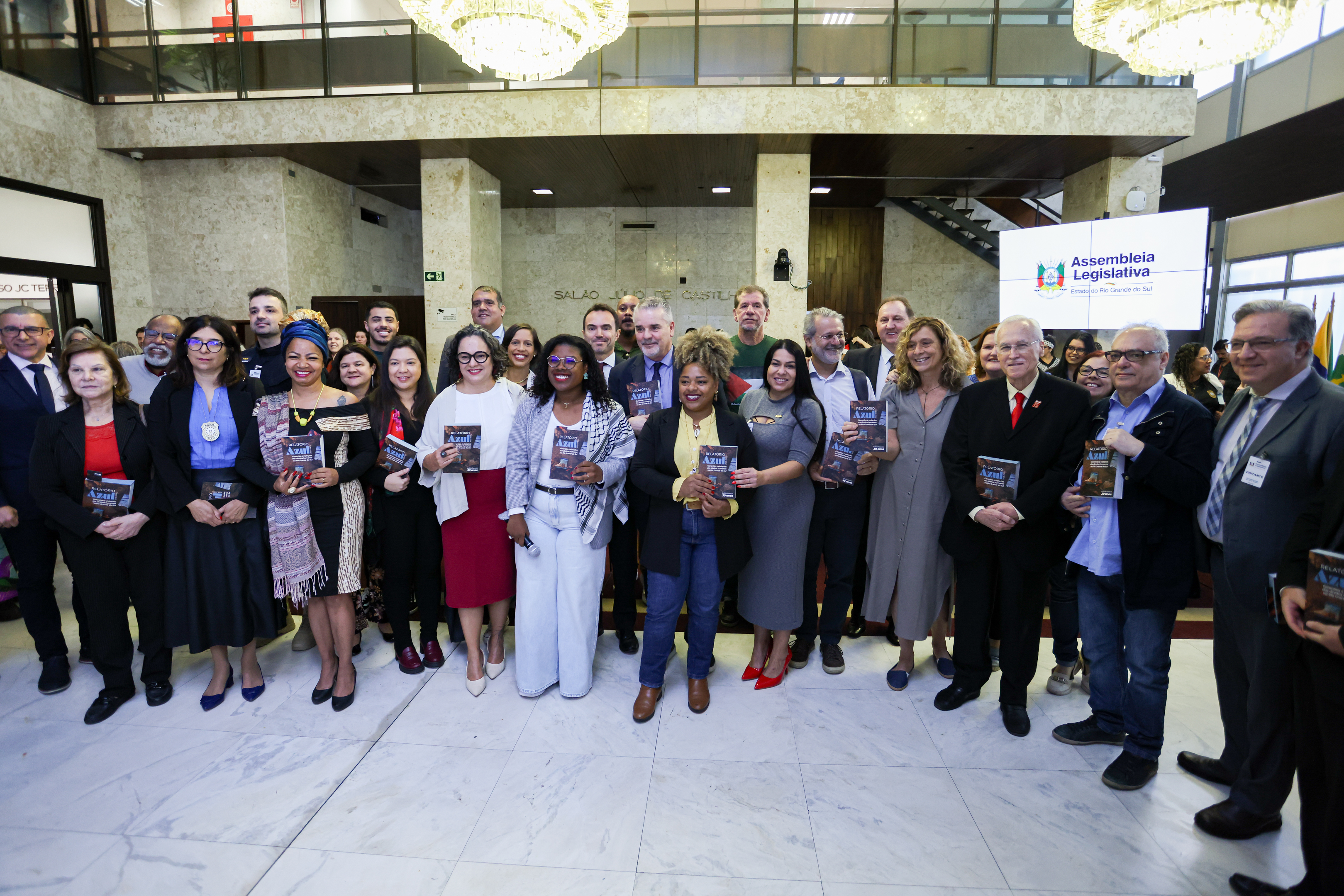 Evento na Assembleia Legislativa. Foto posada dos participantes, segurando a nova edição do Relatório Azul.