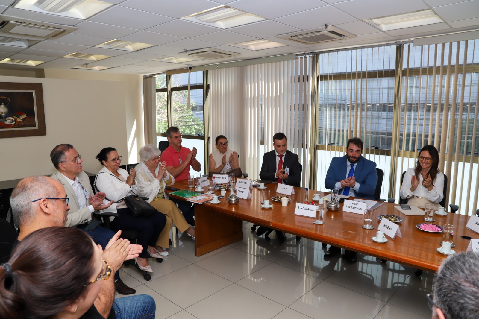 Participantes da mediação ao redor de uma mesa batem palmas.