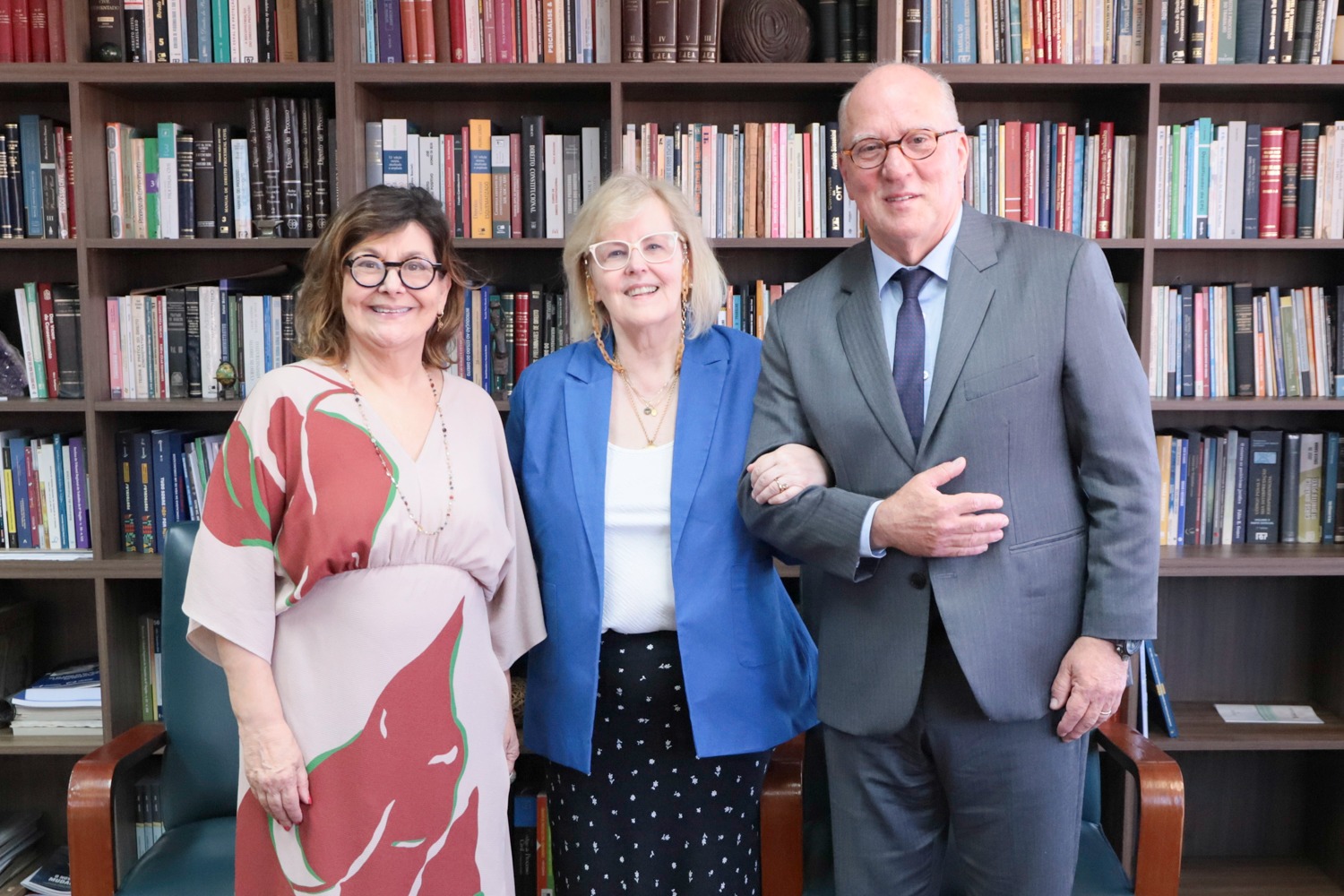 Carmen, Rosa e Ricardo posam para a foto. Os três estão sorrindo. Ao fundo aparece uma estante de livros.