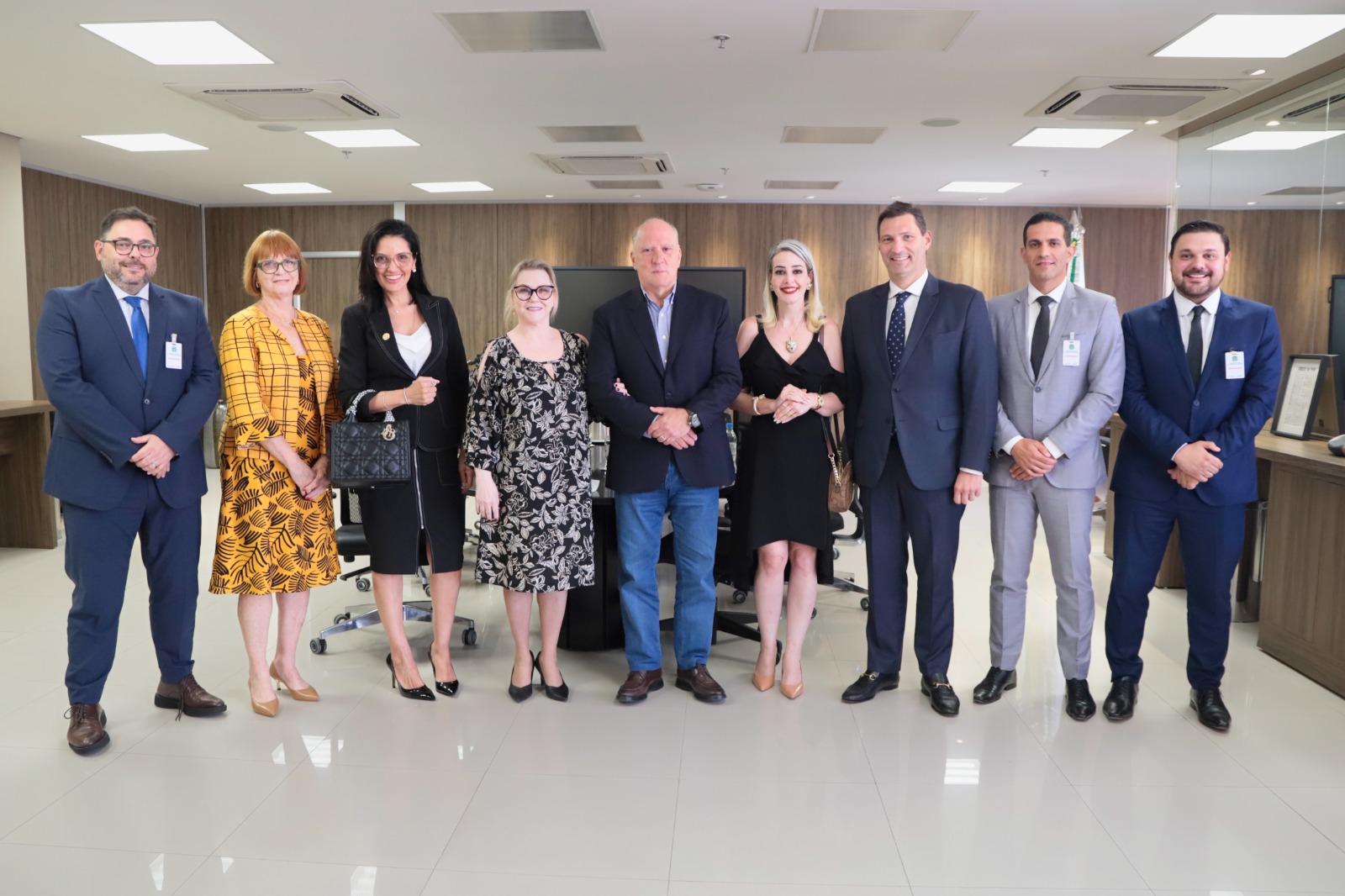 Participantes da reunião possam perfilados para foto. Aparecem nove pessoas de pé, todas estão sorrindo. Ele estão em frente à mesa da reunião.