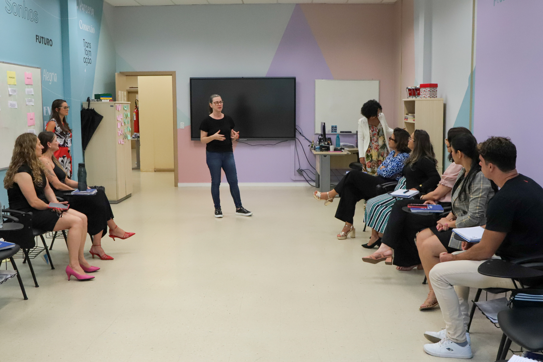Conversa na sala do Projeto Pescar, com a educadora Catia Beulke. Os visitantes estão sentados, e a educadora, em pé.