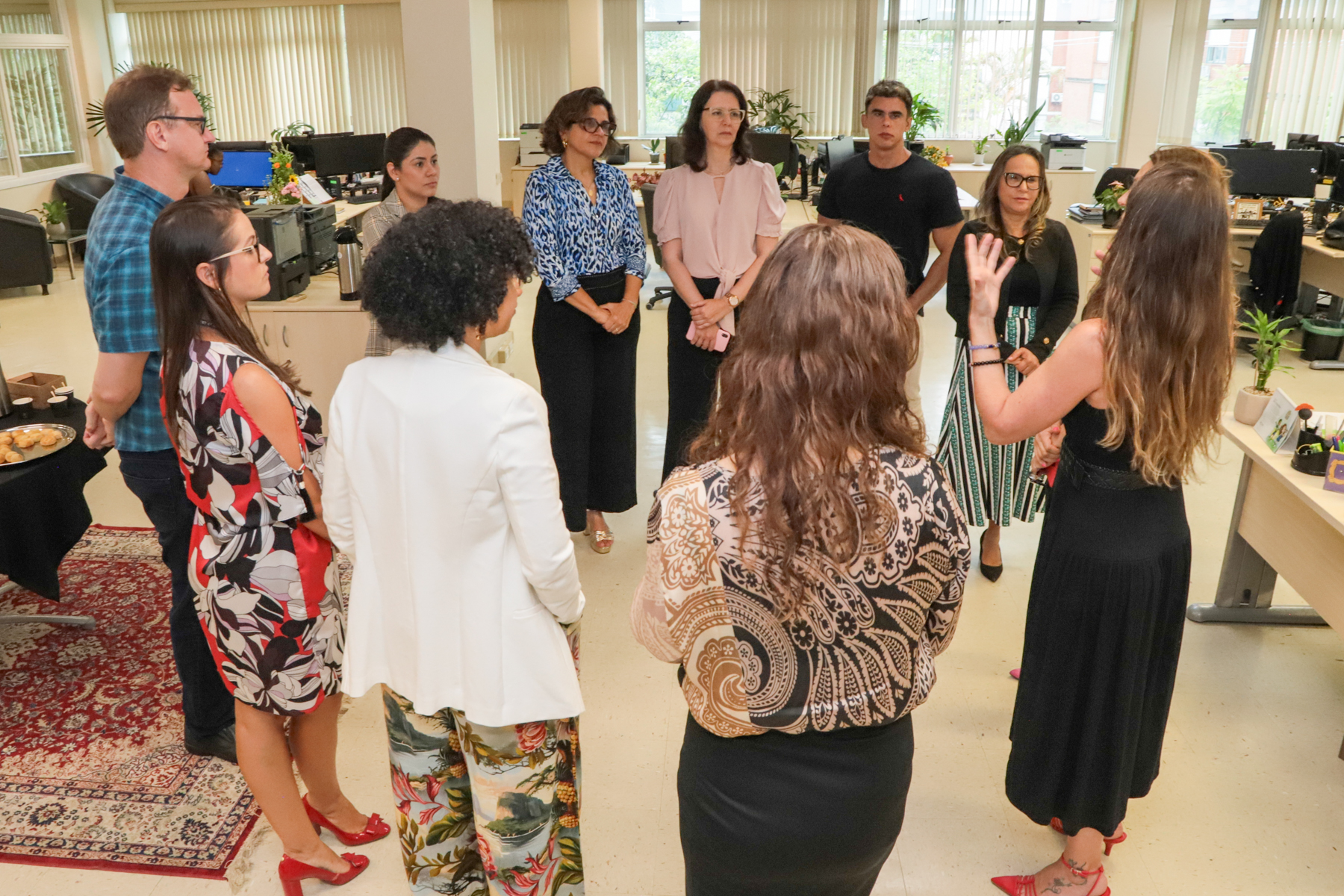 Visitantes e servidores da Ejud estão conversando em pé, formando uma roda, na secretaria da EJud