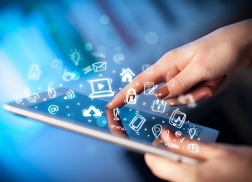 A imagem mostra uma mão interagindo com um tablet, com um fundo desfocado em tons de azul. Do dispositivo, surgem ícones digitais brilhantes desenhados em branco, representando funções como e-mail, Wi-Fi, segurança, localização e redes sociais. A cena transmite uma sensação de tecnologia avançada e conectividade digital.