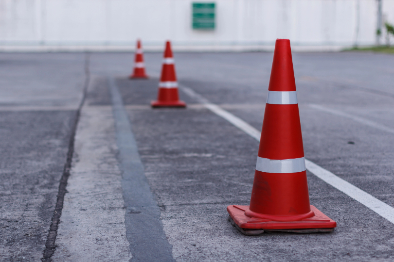 cones de bloqueio de trânsito, na cor laranja, em frente a um portão branco.
