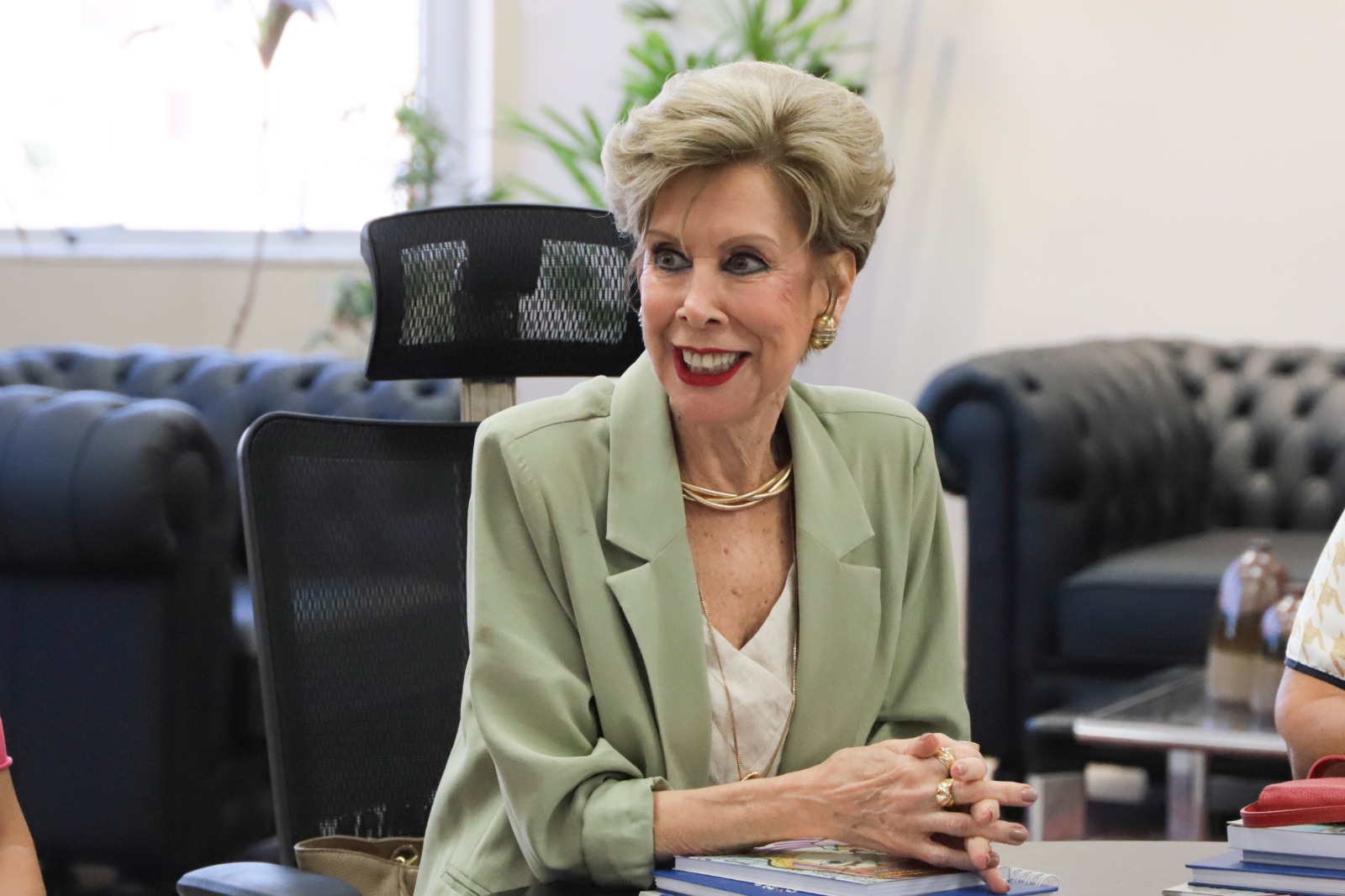 Maria Helena Dornelles é loira, usa blusa branca e casaco verde