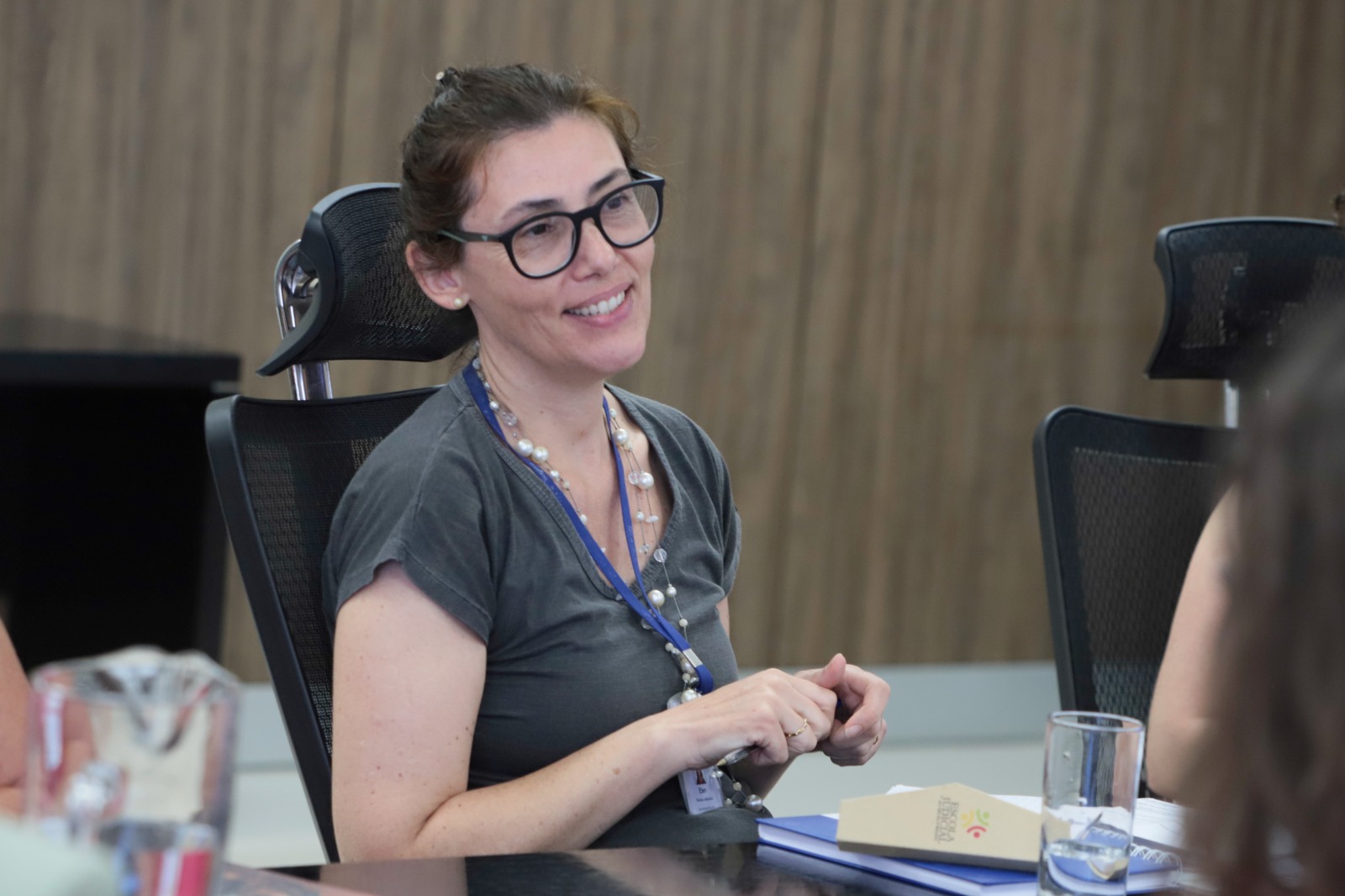 Elen Prezotto é branca, tem cabelo preto liso, usa óculos de armação preta e veste camisa preta. Está falando e sorrindo.