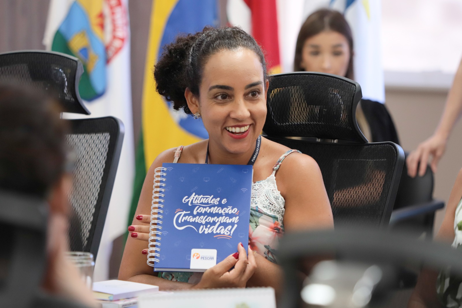 Niura Machado é negra, tem cabelo preto crespo. Está sorrindo e segura um caderno do Projeto Pescar onde se lê "Atitudes e formação transformam vidas".