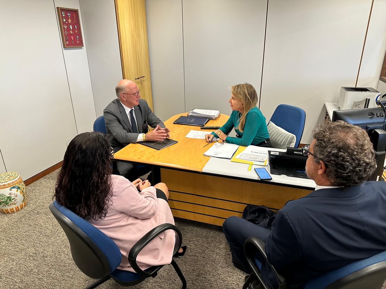Des. Martins Costa reunido com a assessora parlamentar do TST Clara. Juntos na imagem estão os servidores do TRT-RS Diogo e Carolina. Estão numa sala em volta de uma mesa.