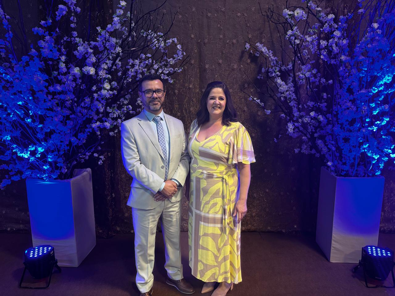 Juiz Clocemar Lemes Silva, titular da 2ª Vara do Trabalho de Estrela, e a reitora da Univates, Evania Schneider. Eles estão posando para uma foto juntos, atrás deles tem dois vasos de plantas brancas sob uma iluminação azul.