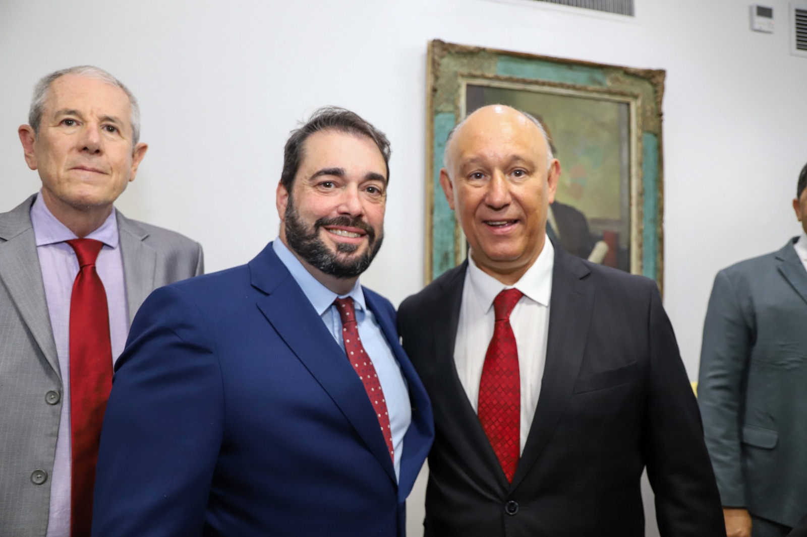 A imagem mostra à esquerda do desembargador Alexandre, que usa terno azul e gravata vermelha. O deputado Pepe está à direita, usando um terno escuro, camisa branca e uma gravata vermelha com um padrão discreto.