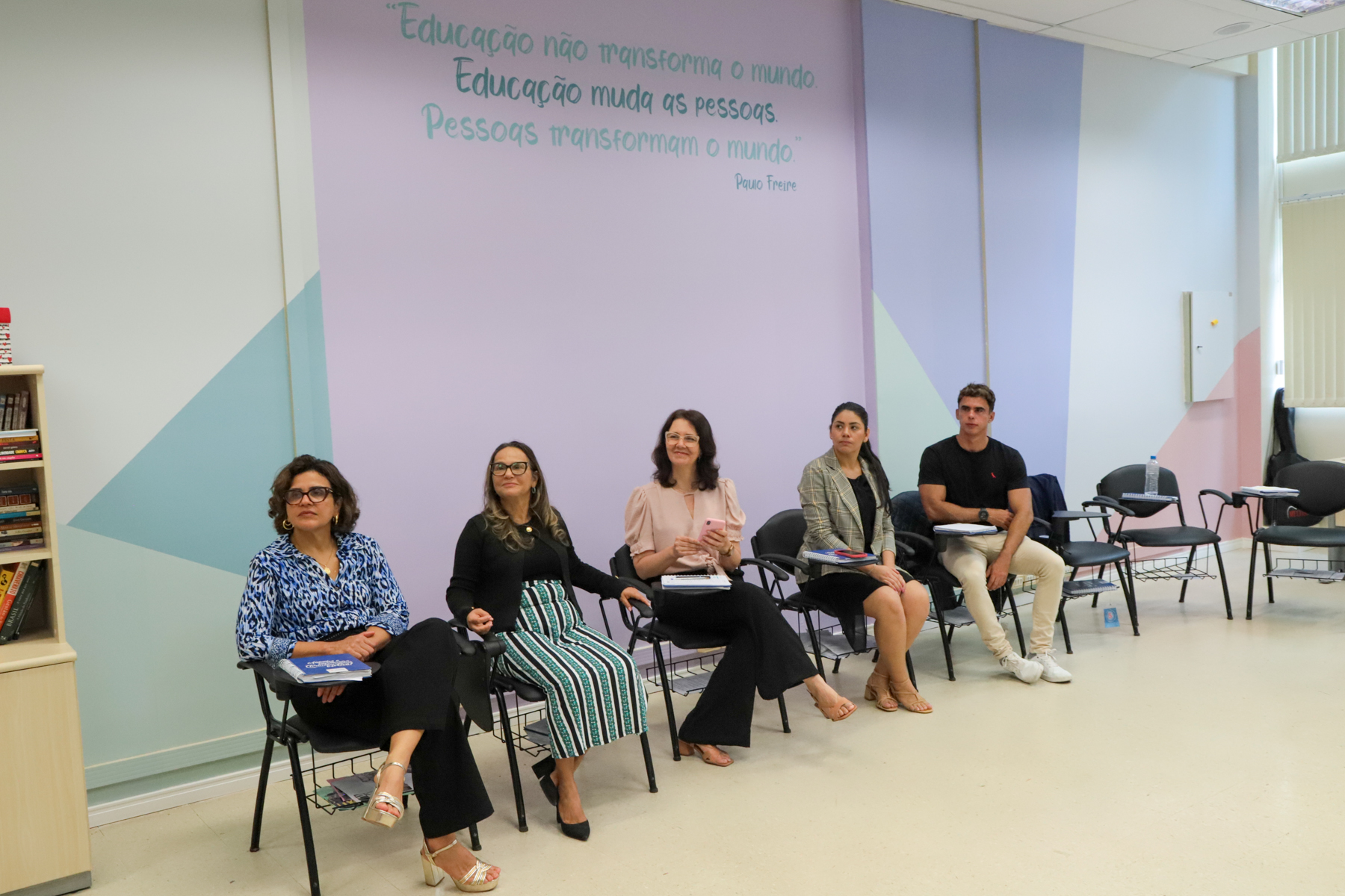 Foto dos visitantes sentados nas classes dos alunos do Projeto Pescar, na sala de aula.