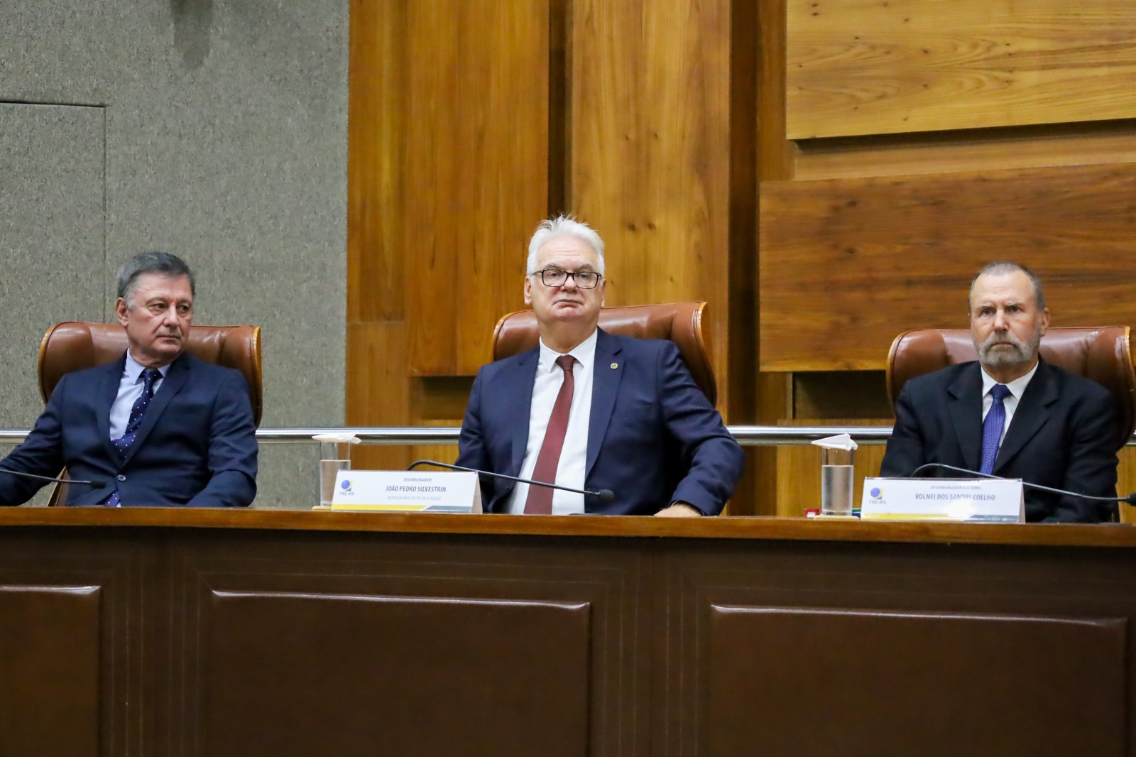 A imagem mostra o desembargador João Pedro Silvestrin, ao centro, na mesa de autoridades, ao lado de outras duas pessoas.