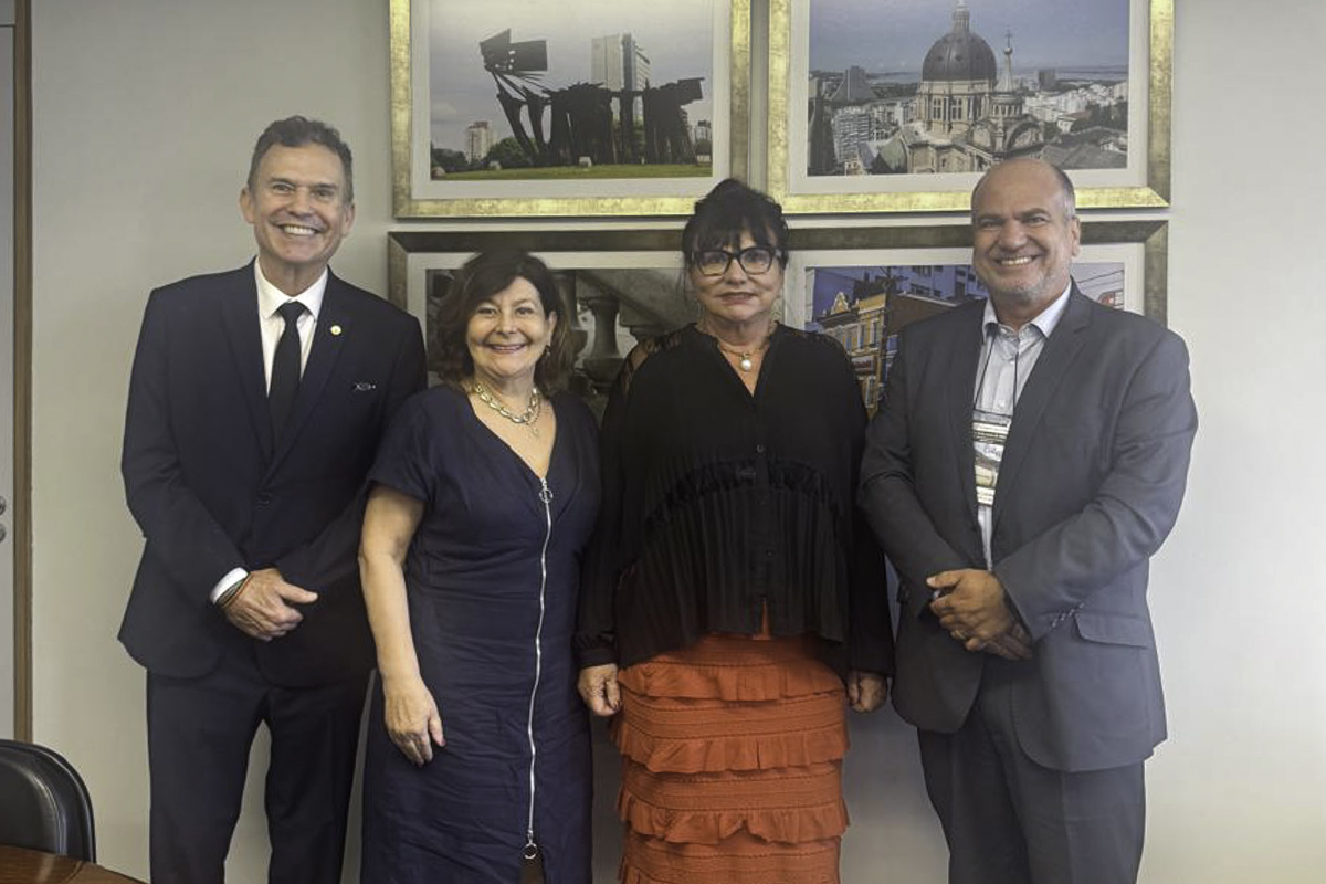 Magistrados e magistradas posam para a foto sorrindo. Na parede ao fundo há quatro fotografias emolduradas com pontos turísticos de Porto Alegre. 