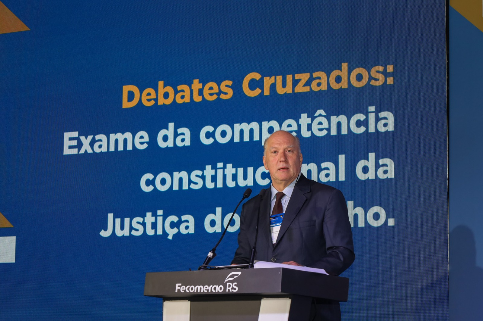 Presidente discursando com o tema da palestra ao fundo