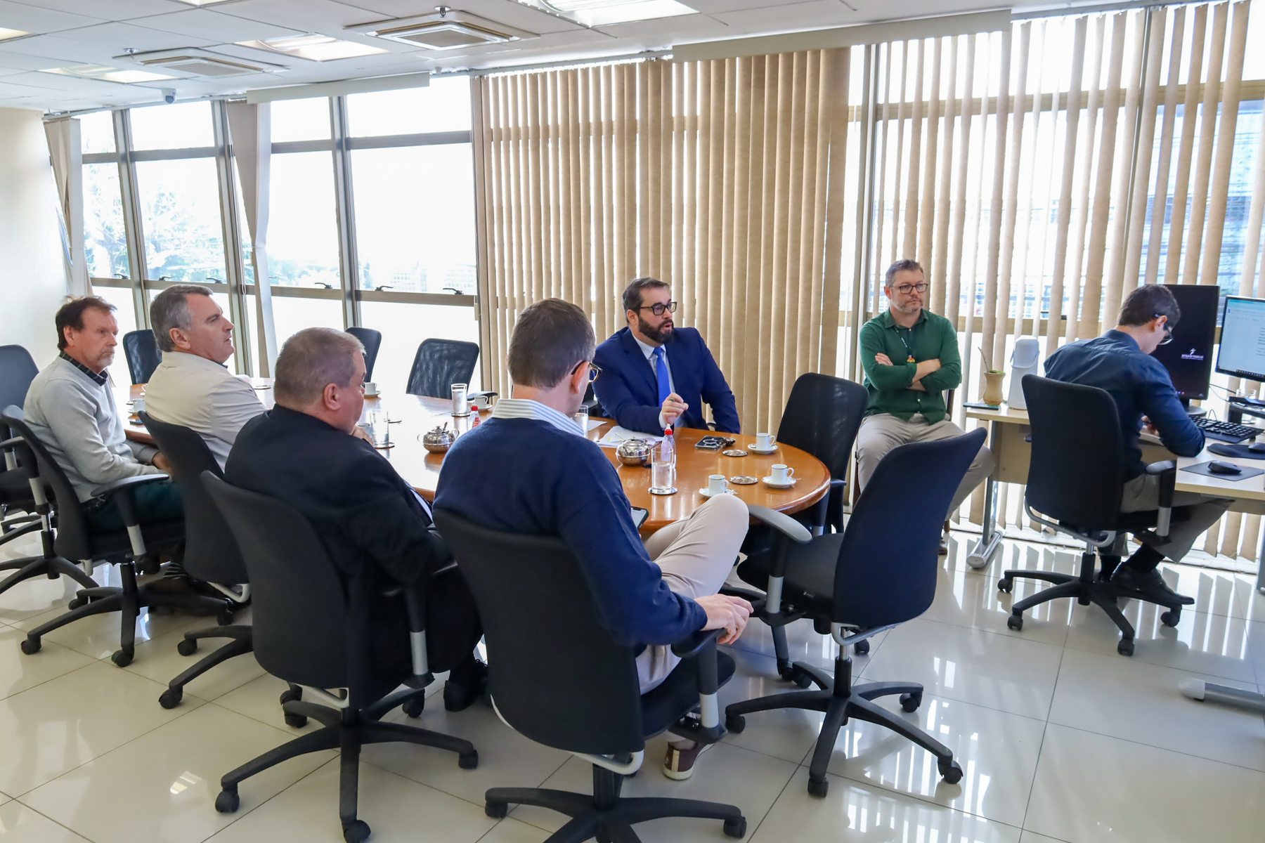 Foto da audiência no TRT-RS, mostrando pessoas sentadas à mesa de reuniões.