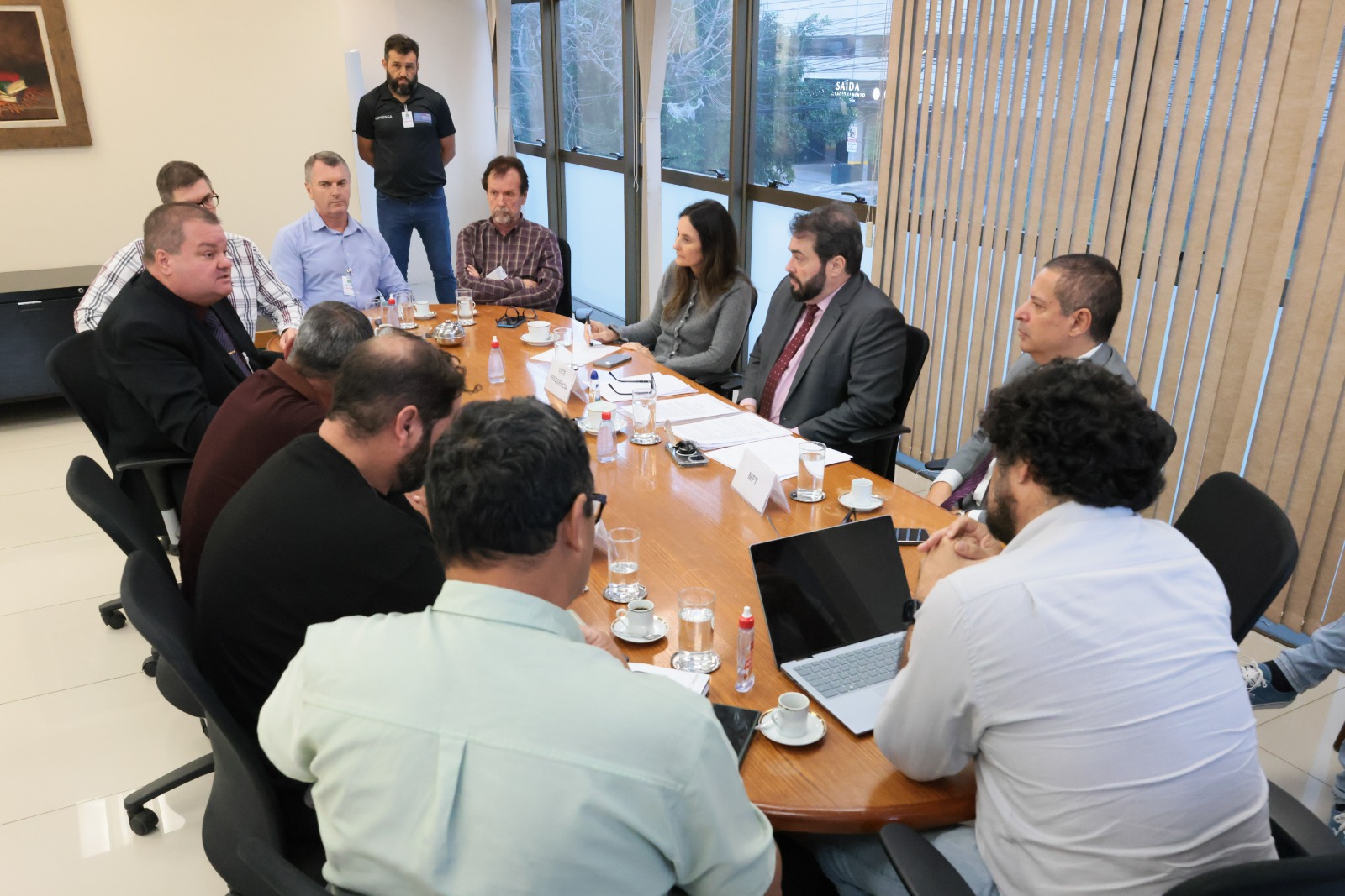 Pessoas na mesa de negociação, vistas por outro ângulo, com a janela ao fundo.