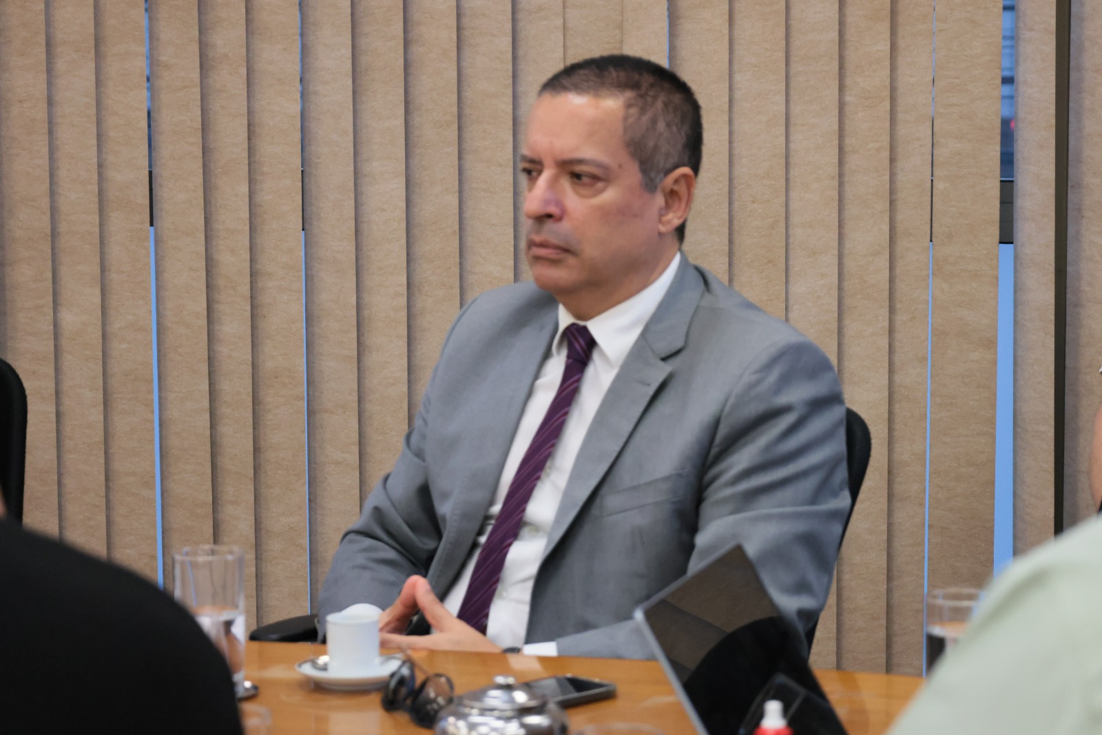 Marcelo Goulart é branco, de cabelo escuro curto. Usa blazer cinza, camisa branca e gravata roxa listrada.