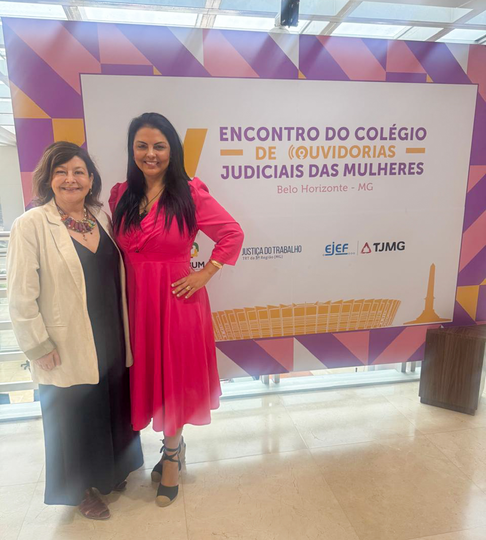 Desas. Carmen e Tânia, em frente ao backdrop do evento