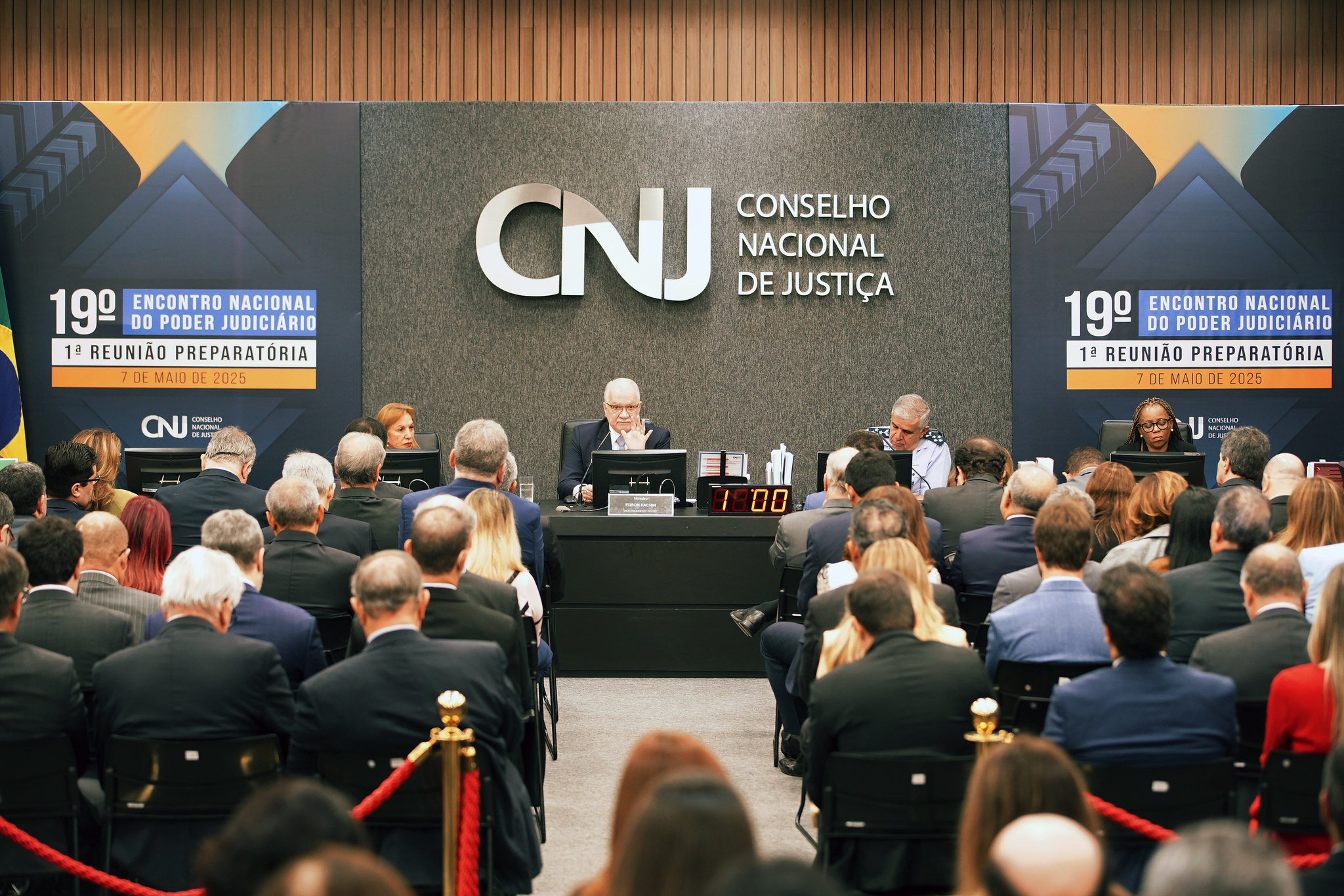Foto em ângulo aberto da reunião, mostrando mesa ao fundo e, no primeiro plano, a plateia de costas