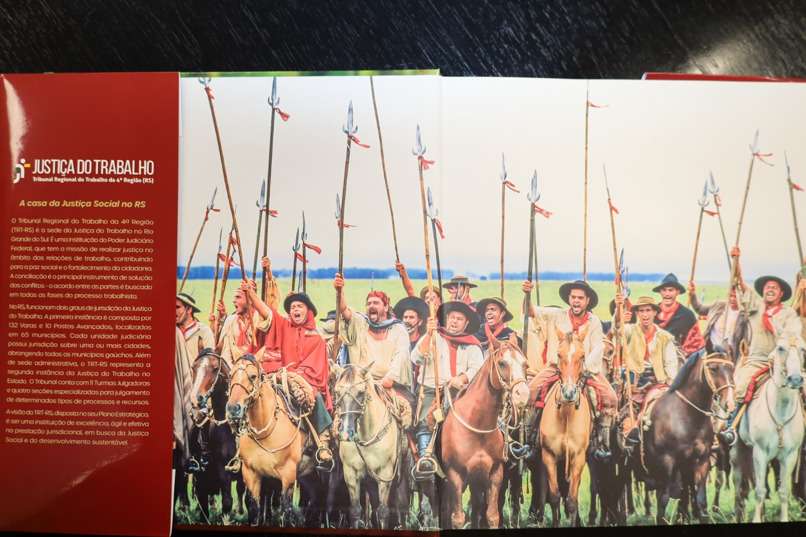 Foto da parte interna de livro com participação do TRT-RS. Mescla de texto e imagem. Com sobrecapa com informações da Justiça do Trabalho.
