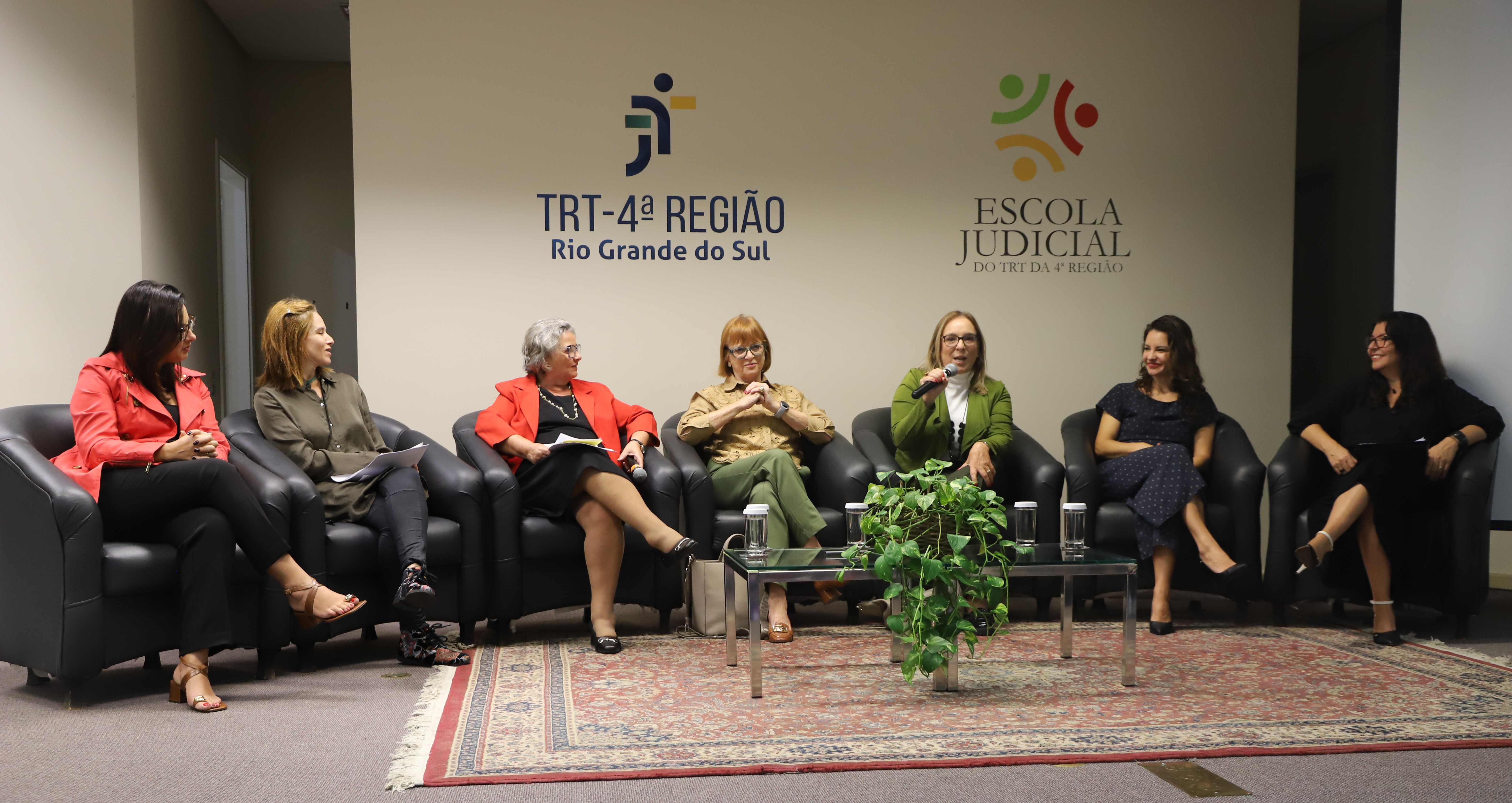 Magistradas e servidores sentadas em poltronas no palco