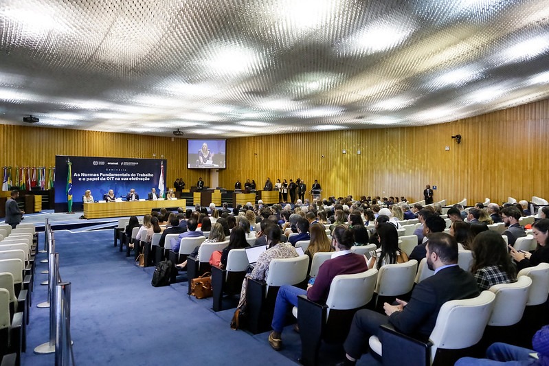 Auditório do TST, com a fila de cadeiras do público em primeiro plano e a mesa oficial ao fundo.