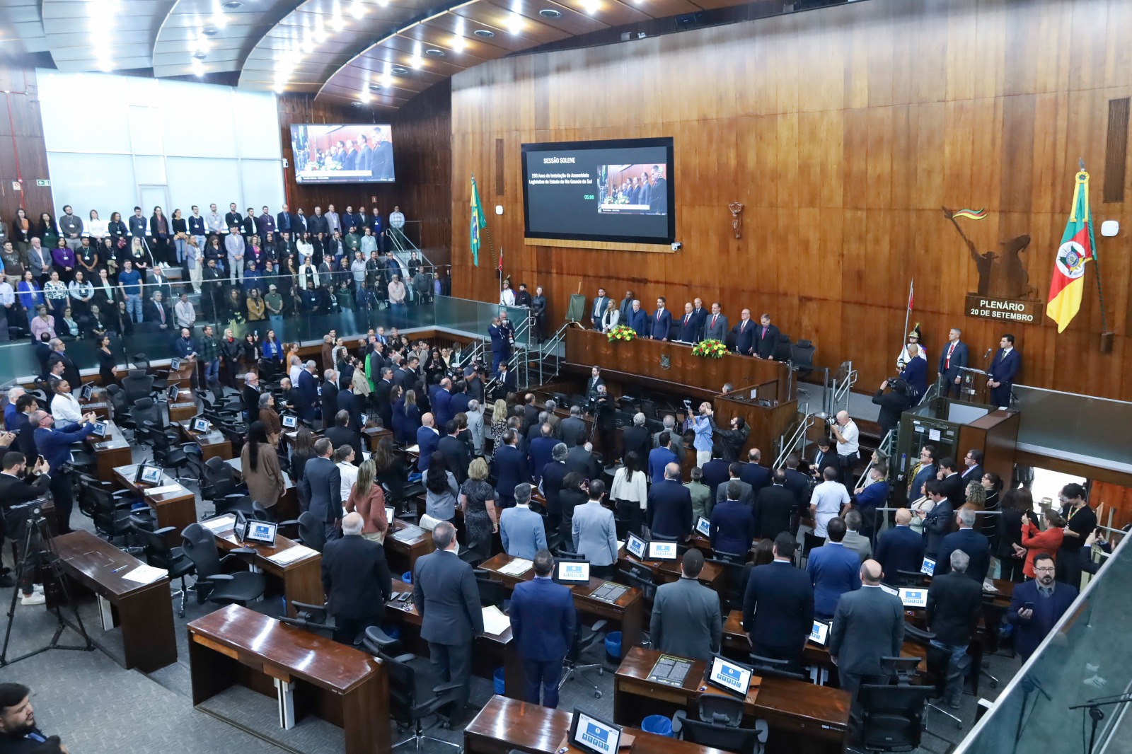 Foto geral do plenário, com as mesas dos parlamentares em primeiro plano e a mesa oficial ao fundo