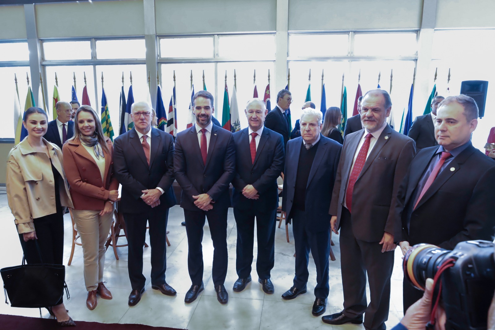 Oito pessoas perfiladas posam para a foto. Ao fundo aparecem diversas bandeiras