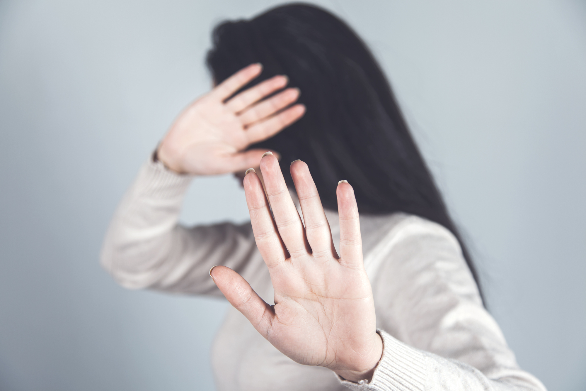 Mulher com expressão de defesa cobre o rosto com as mãos, simbolizando recusa, medo ou tentativa de proteção.