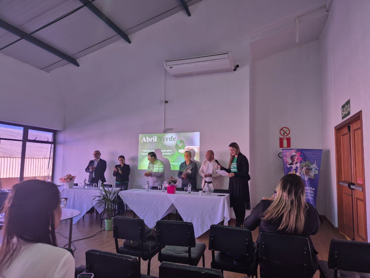 Fotografia durante a palestra do abril verde, há 6 pessoas na imagem sendo 4 homens e 2 mulheres e todos estão de pé.