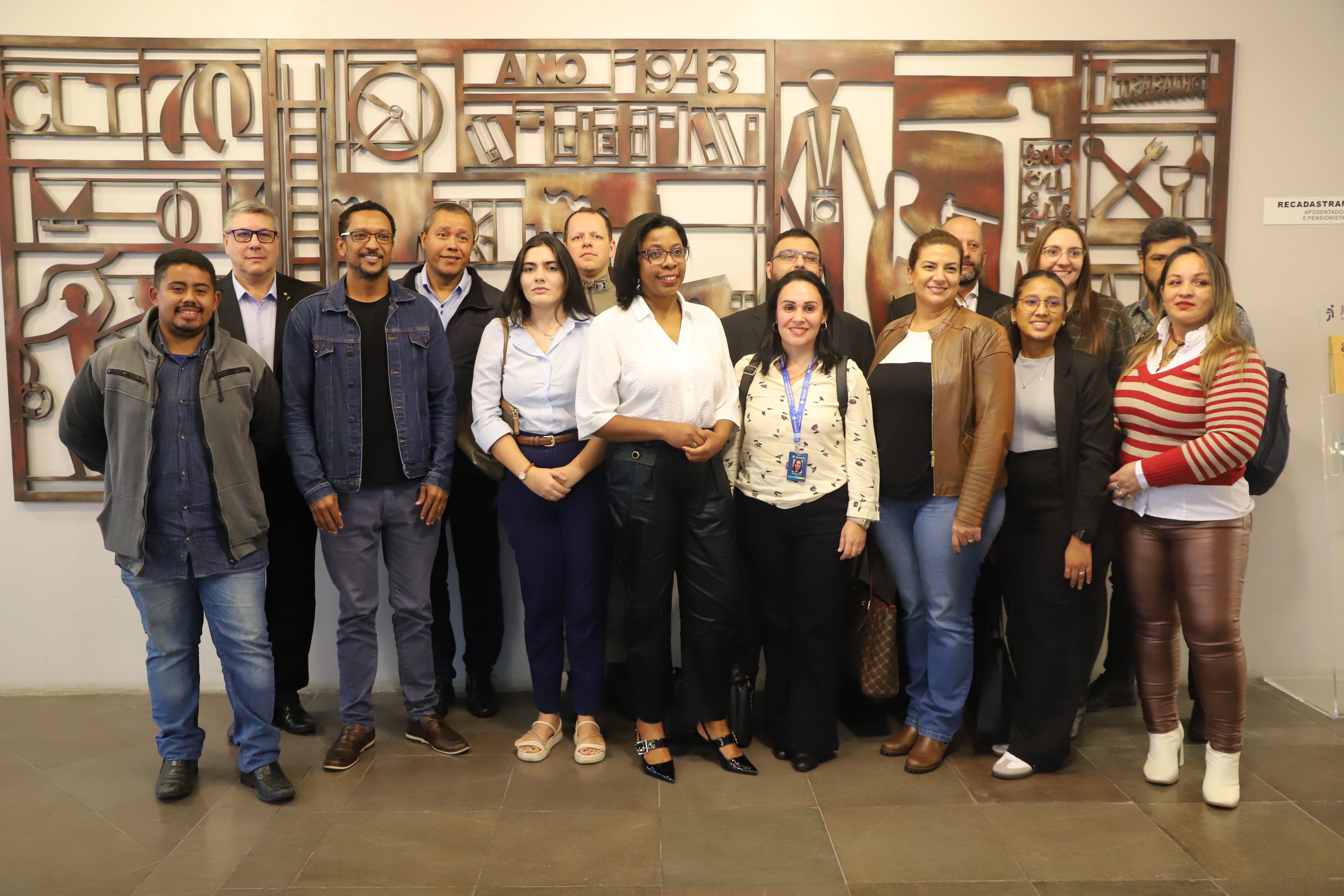 Grupo de alunos e professores reunidos no saguão, posando em frente a um mural artístico com símbolos da CLT.