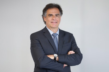 Luiz Philippe é branco e de cabelos grisalhos. Veste blazer cinza escuro com camisa e gravata em tons de azul claro. Está de pé, de braços cruzados, sorrindo para a foto.